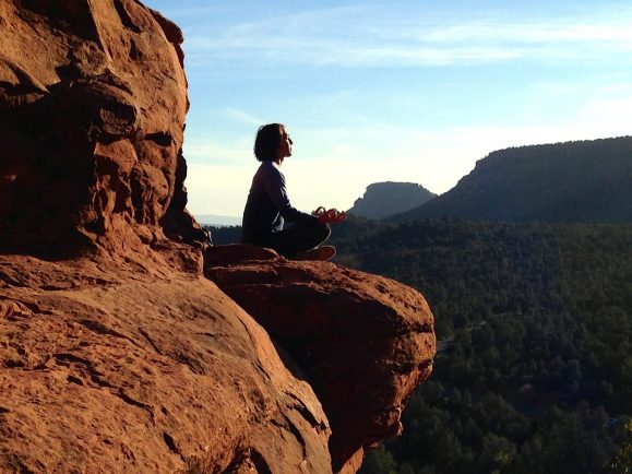 Girl learning Buddhist meditation in natural, beautiful cliff landscape.