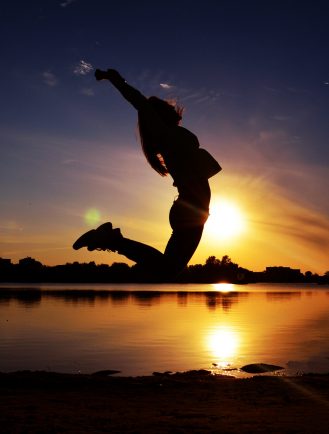 Girl jumping in front of a decorative sunset after finishing a book